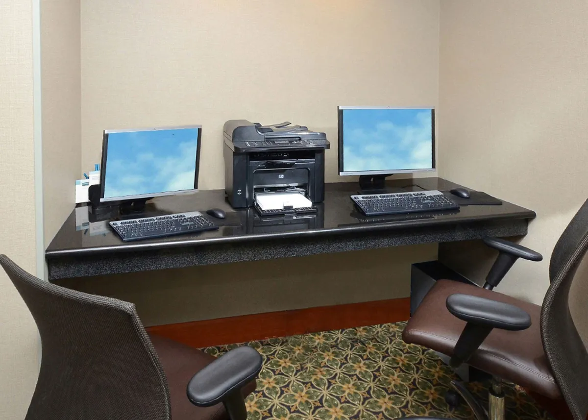 A well-equipped workspace with two computer monitors, a printer, a dark countertop, and comfortable office chairs. The area is designed for productivity, with easy access to technology and space for focused work.