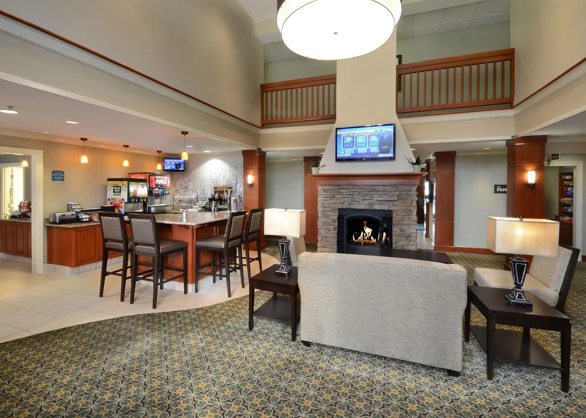 This image features a comfortable and inviting interior lounge area with a fireplace, bar seating, and a cozy arrangement of chairs and a sofa. Guests are seen relaxing, socializing, and enjoying drinks, with a television visible above the fireplace. The scene exudes a sense of warmth, comfort, and communal living.