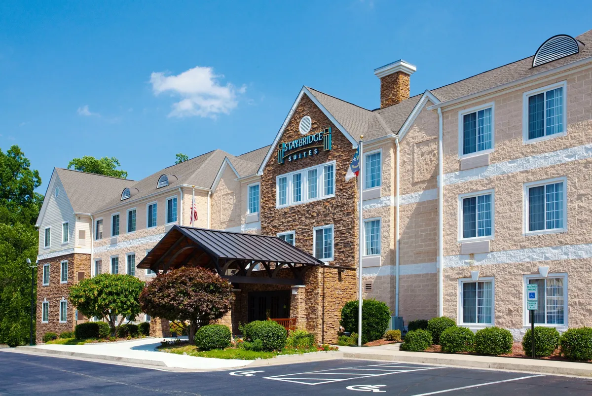 The exterior view of the property, showcasing the entrance awning, stone facade, large windows, and landscaped greenery. The space is welcoming and projects a sense of security and professionalism, hinting at the transparent, reliable service that begins at check-in.