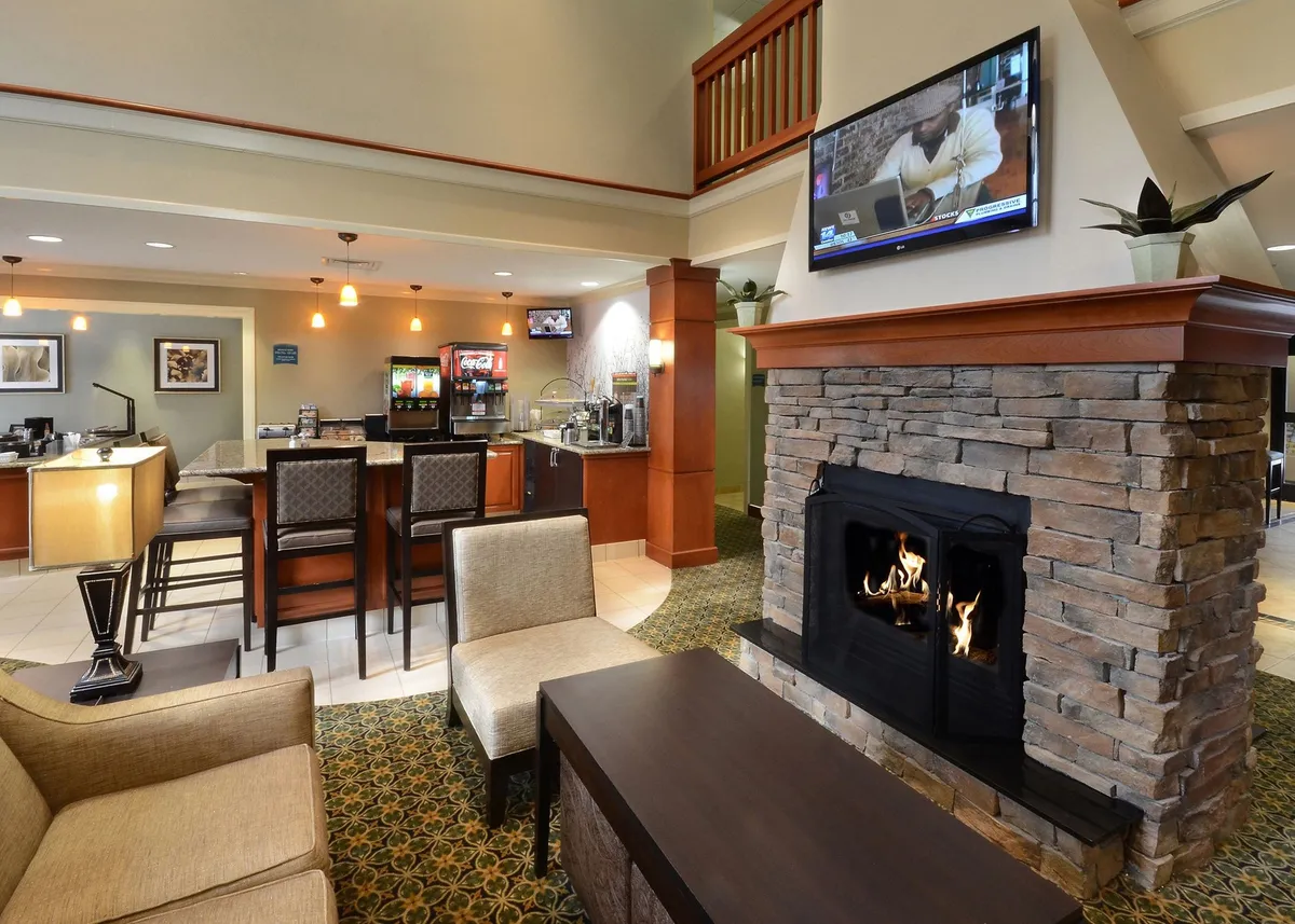 A warmly lit lounge area featuring a modern fireplace, a bar area, comfortable seating, and a television. The ambiance is cozy and inviting, suggesting a communal space where guests can relax, socialize, or unwind with a drink after a busy day. The decor and amenities reflect a high standard of comfort.