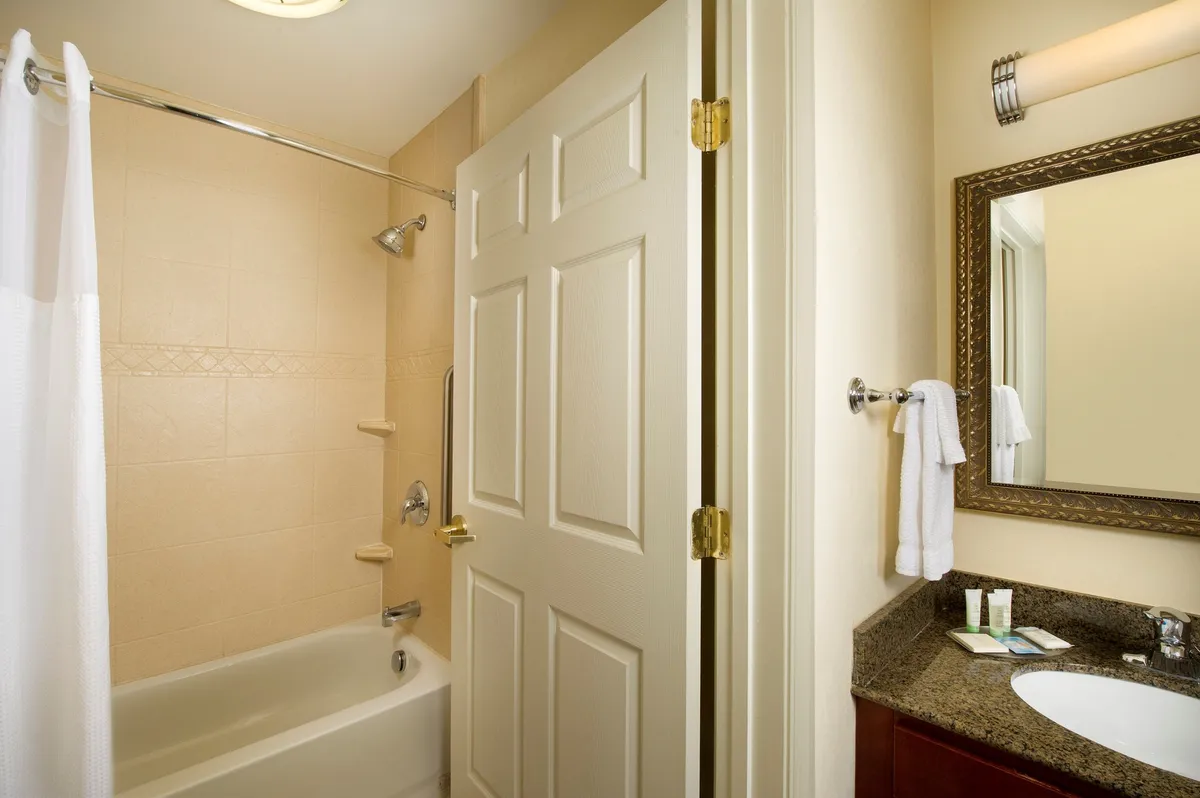 A bright, clean bathroom with a large mirror, modern sink, bathtub, and plush towels. The setup suggests thoughtful attention to guest needs, offering a refreshing space for grooming and relaxation.